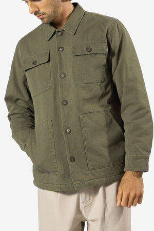 A man in a Mr Simple Stockyard Sherpa Jacket, olive green regular fit with front pockets, over light-colored pants stands against a white background, his head slightly turned down and to the left.