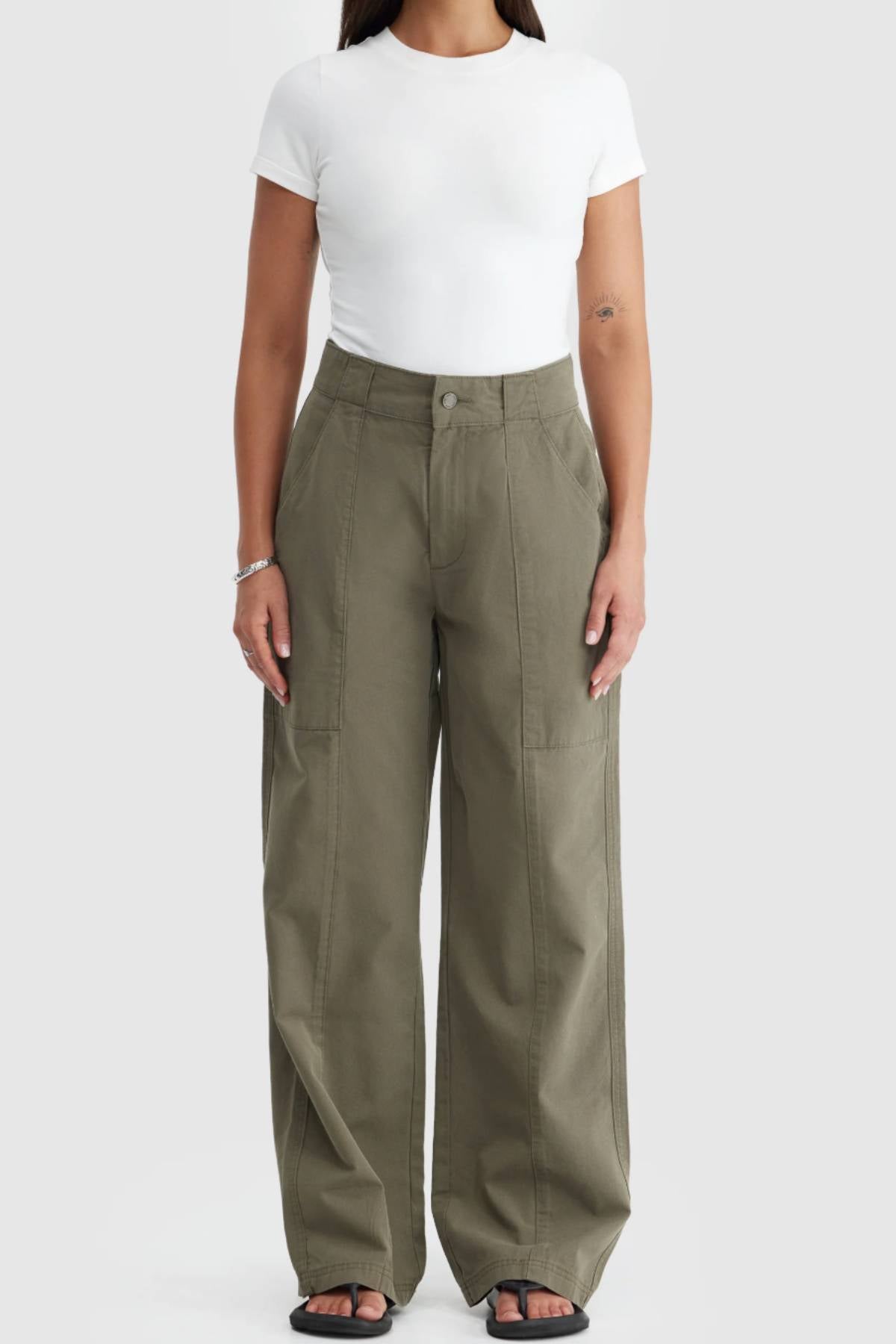 Wearing a fitted white short-sleeve tee and ORTC Avery Front Seam Pants—cotton tencel, high-waisted with large front pockets, designed in Australia—the person stands against a plain light background.