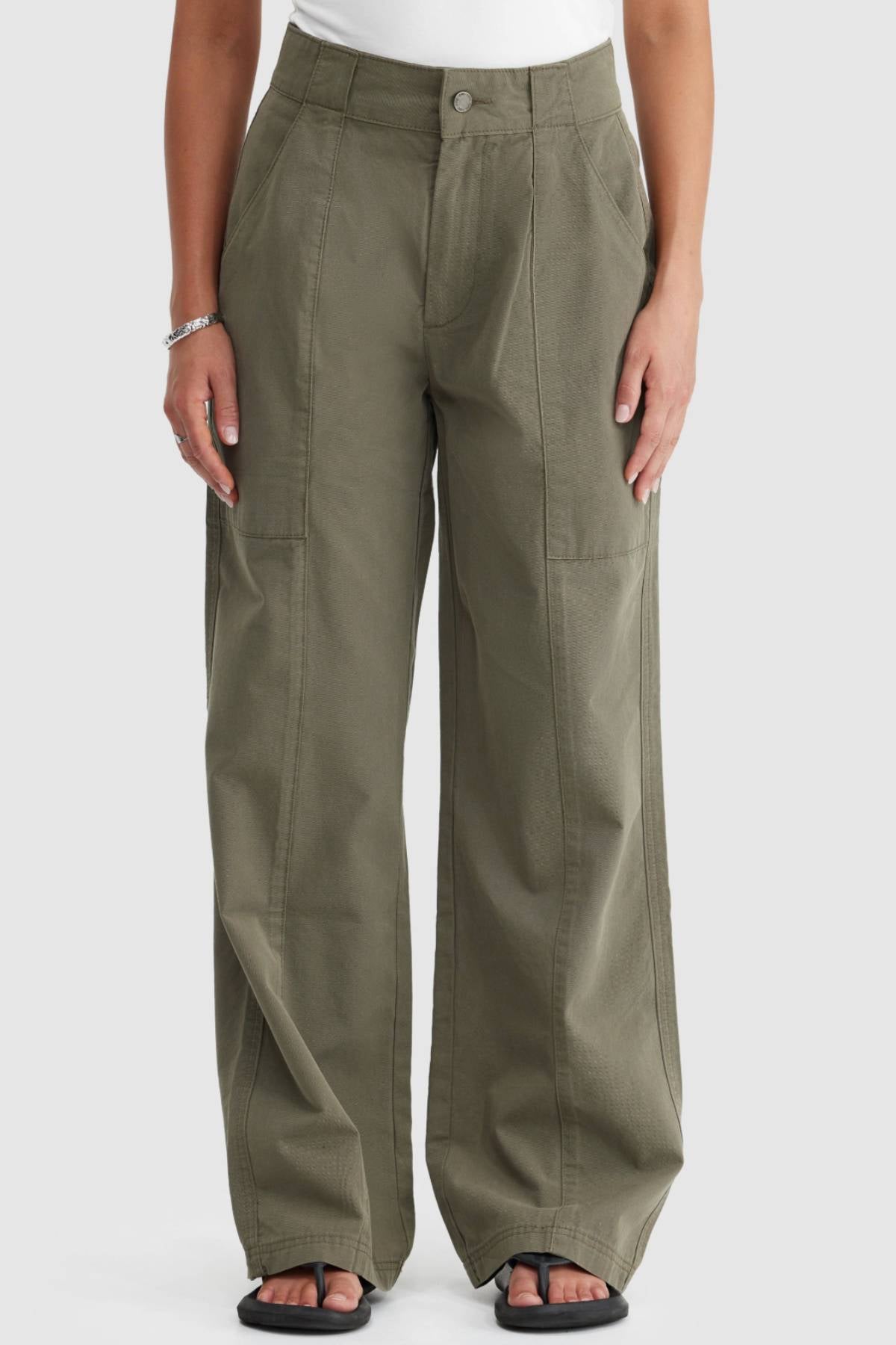A person wears ORTC Avery Front Seam Pants—high-waisted, olive green, crafted from cotton tencel and designed in Australia—with a white top, black sandals, and a bracelet. The image displays the pants from the waist down.