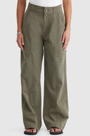 A person wears ORTC Avery Front Seam Pants—high-waisted, olive green, crafted from cotton tencel and designed in Australia—with a white top, black sandals, and a bracelet. The image displays the pants from the waist down.