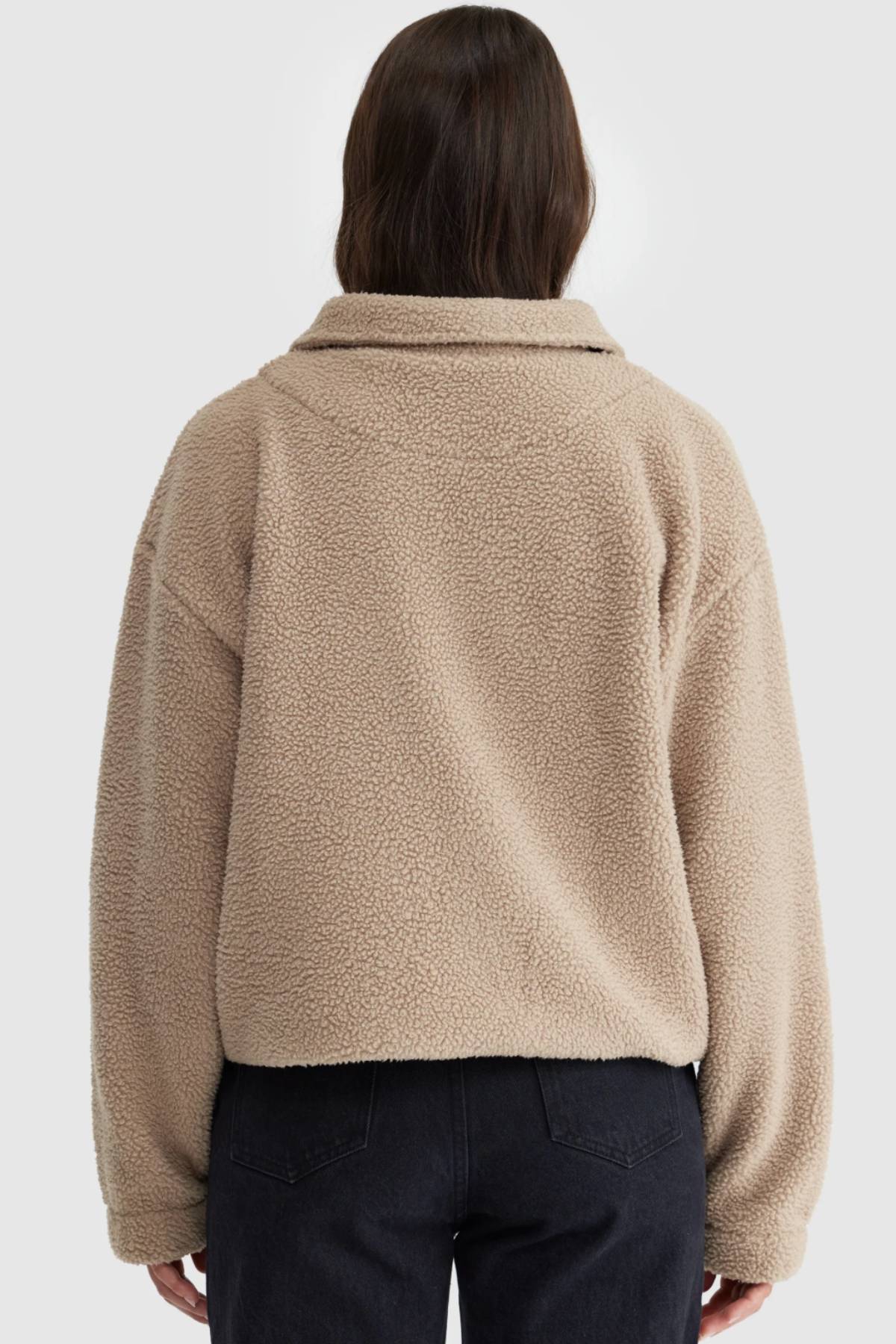 A person with long brown hair, seen from behind, is wearing the ORTC Georgia Sherpa Jacket in beige and black jeans against a plain light background.