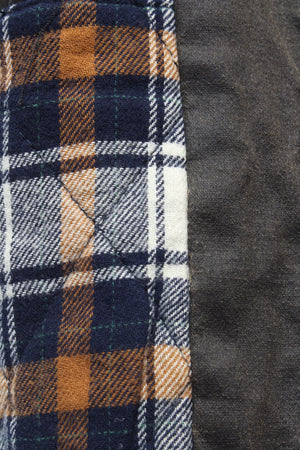 Close-up of a patchwork pattern on the Outback Heritage Jacket, showcasing a blue, white, and orange plaid cotton/polyester fabric stitched next to solid gray fabric. The vivid textures and colors are clearly visible, with noticeable stitching along the edge of the plaid providing both style and durability.