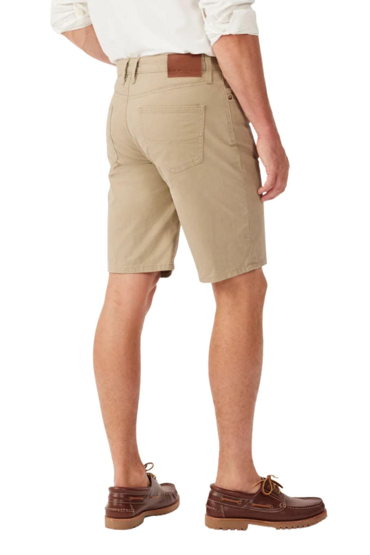 A man wearing a white shirt, RM Williams Nicholson Shorts in tan Australian stretch cotton twill, and brown boat shoes stands with his back to the camera; the regular fit shorts have back pockets and a brown leather waistband patch.