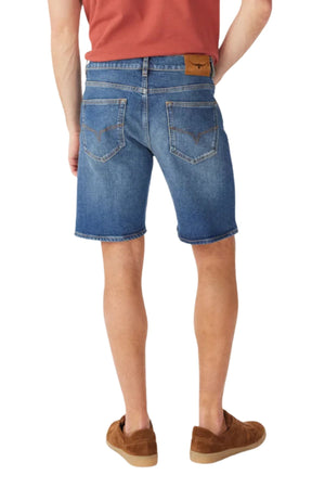 A person stands with their back to the camera against a white background, wearing RM Williams Nicholson Shorts in blue Australian Good Earth Cotton, paired with a red shirt and brown shoes.