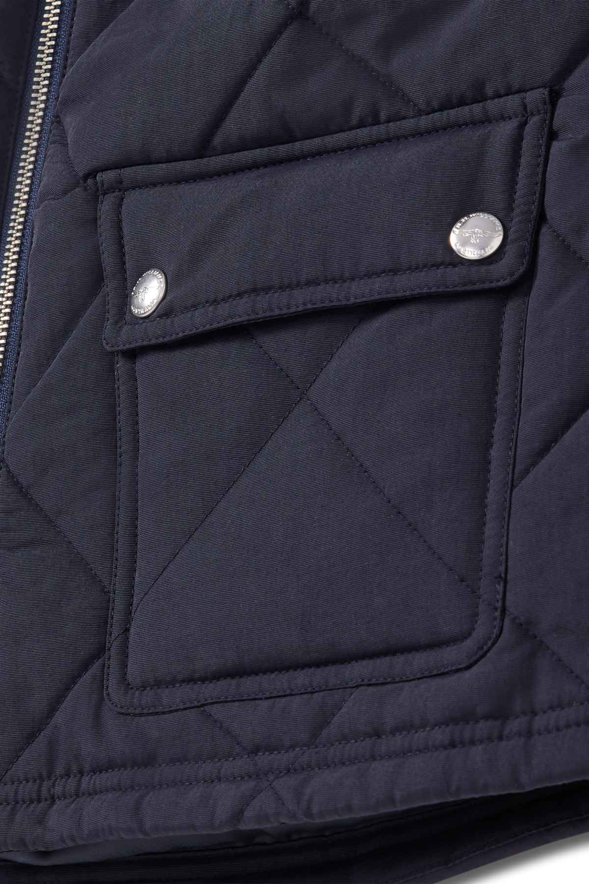 Close-up of the RM Williams Willippa Vest showing its dark quilted design with a flap pocket, two metallic snap buttons, and visible stitching details.