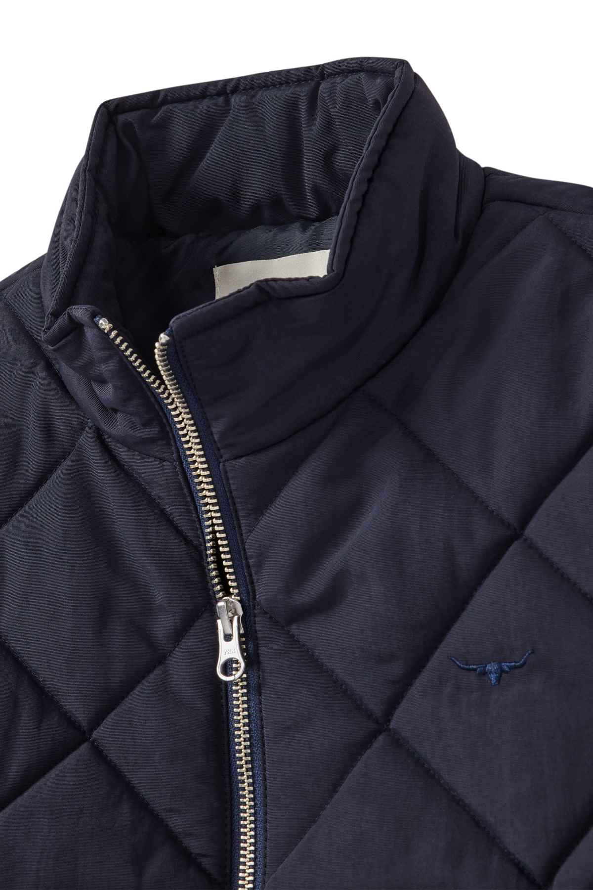 A close-up of the RM Williams Willippa Vest, a dark blue quilted piece with diamond-shaped stitching, silver zipper, high collar, recycled nylon fabric, and an embroidered longhorn logo on the chest.