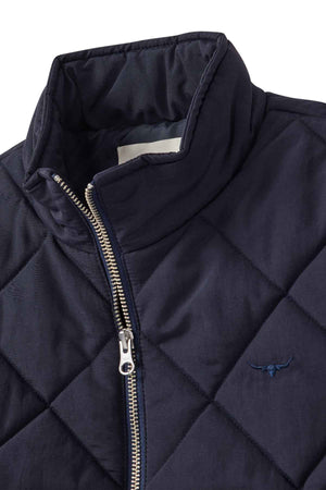 A close-up of the RM Williams Willippa Vest, a dark blue quilted piece with diamond-shaped stitching, silver zipper, high collar, recycled nylon fabric, and an embroidered longhorn logo on the chest.