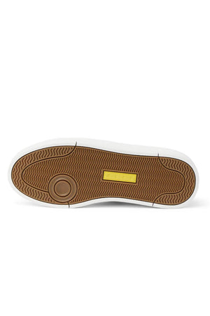 The image shows the bottom view of the Reef Bom Dia Shoe, featuring a brown textured rubber sole with a circular design at the heel, a yellow rectangular label at midfoot, white outer edge, and all-day comfort from its cushioned footbed.