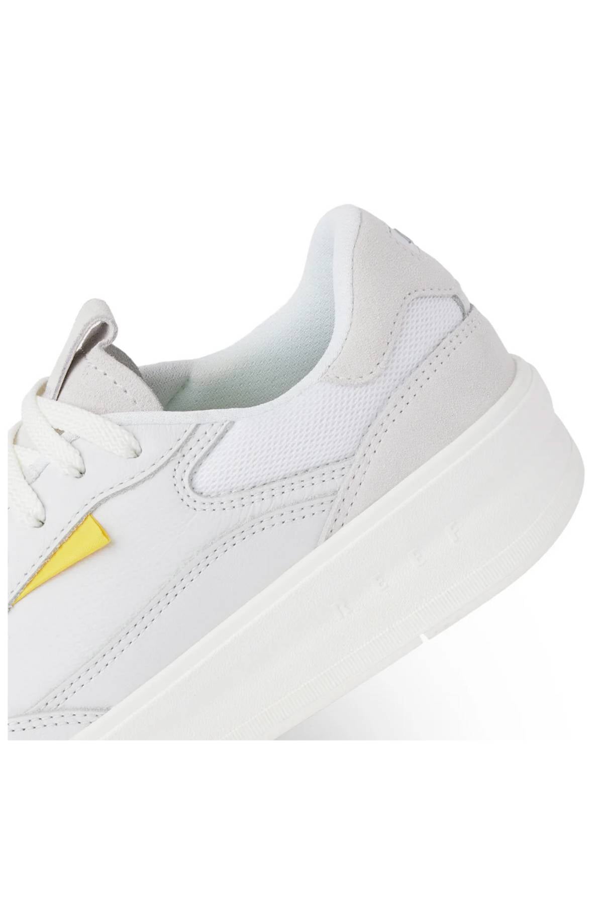 Close-up of the Reef Bom Dia Shoe, a white sneaker with a thick sole, light grey suede accents, and a small yellow lightning bolt on the side. Features a cushioned footbed for all-day comfort. Shown against a plain white background.