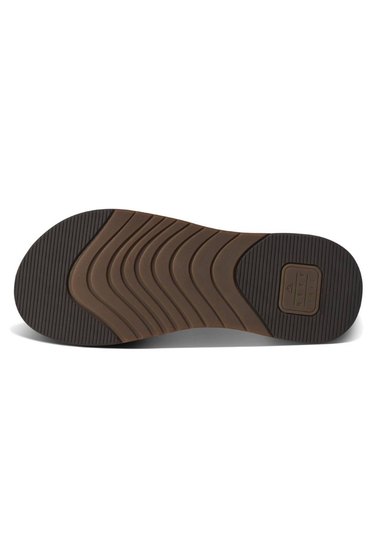 The image displays the sole of the REEF Cushion Norte sandal, showing brown and dark brown rubber with wavy, textured grooves for grip. A rectangular REEF-branded label appears near the heel.
