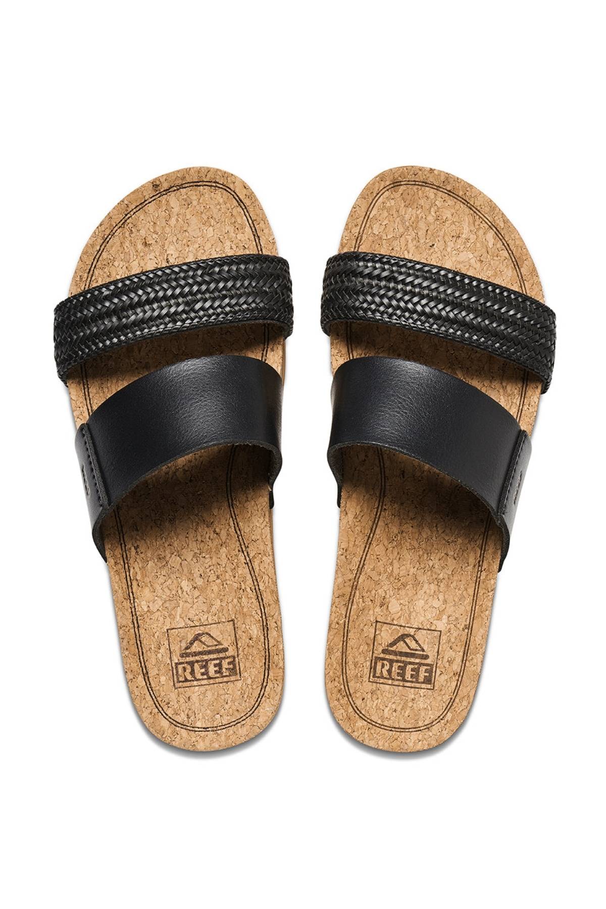 A pair of REEF Cushion Vista Hi slip-on sandals with black leather straps, cushioned slides design, cork footbeds, and REEF logo on the insoles for arch support and comfort.