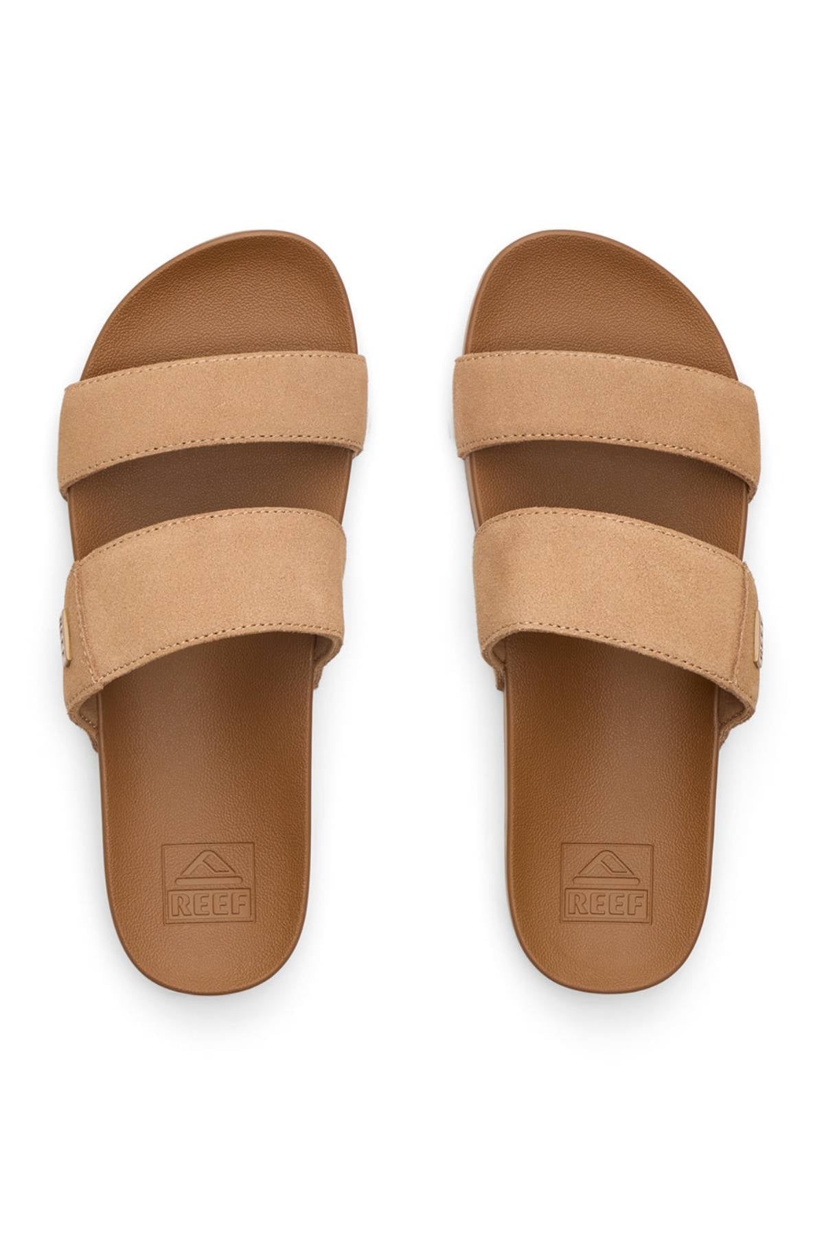 A pair of tan REEF Cushion Vista Stevie slip-on sandals with two wide suede straps and brown cushioned footbeds, viewed from above. The "REEF" logo is stamped near each heel.