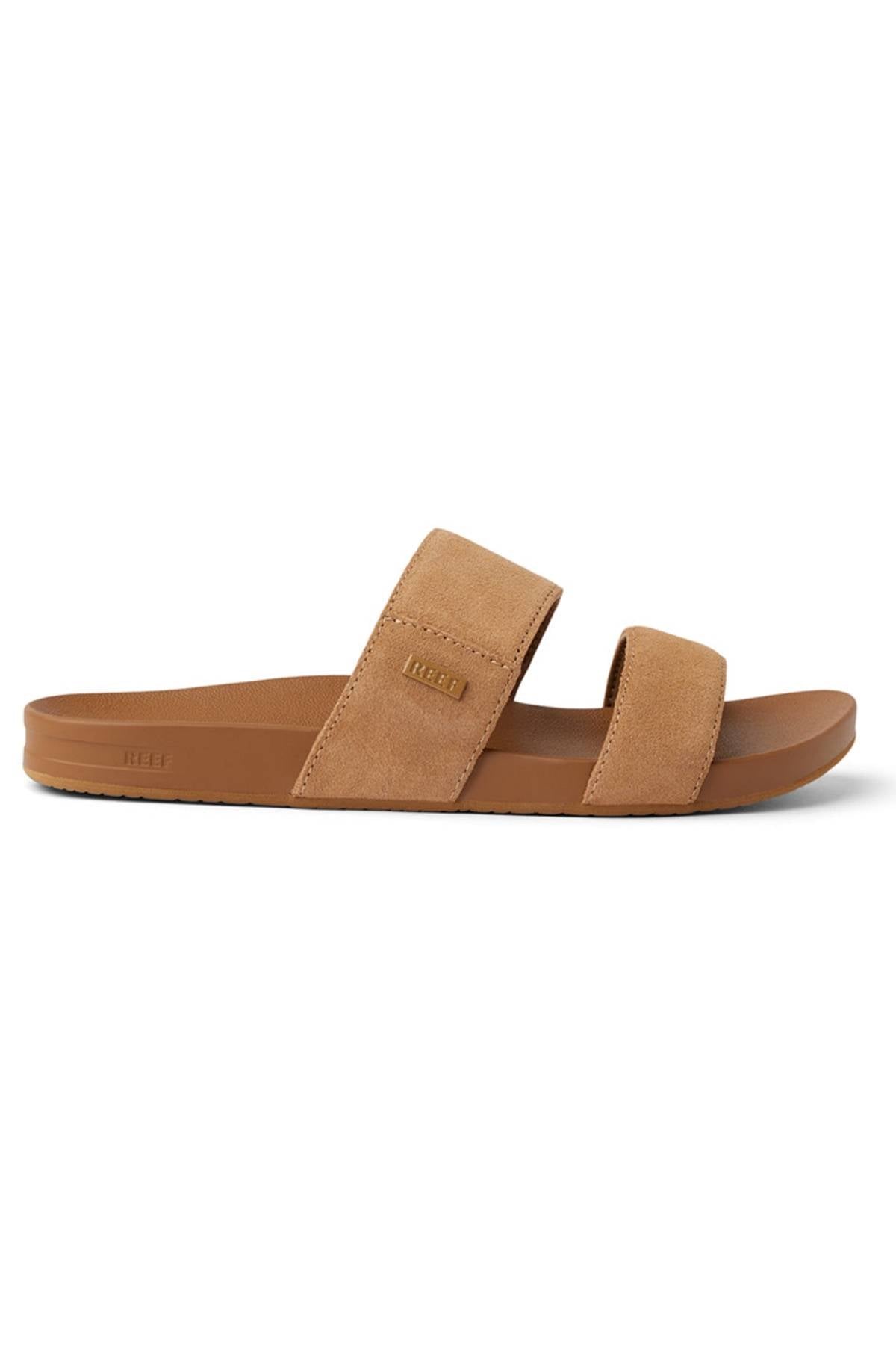 The REEF Cushion Vista Stevie is a tan slide sandal with two wide suede straps, a flat sole, and subtle arch support, shown in side profile against a white background.