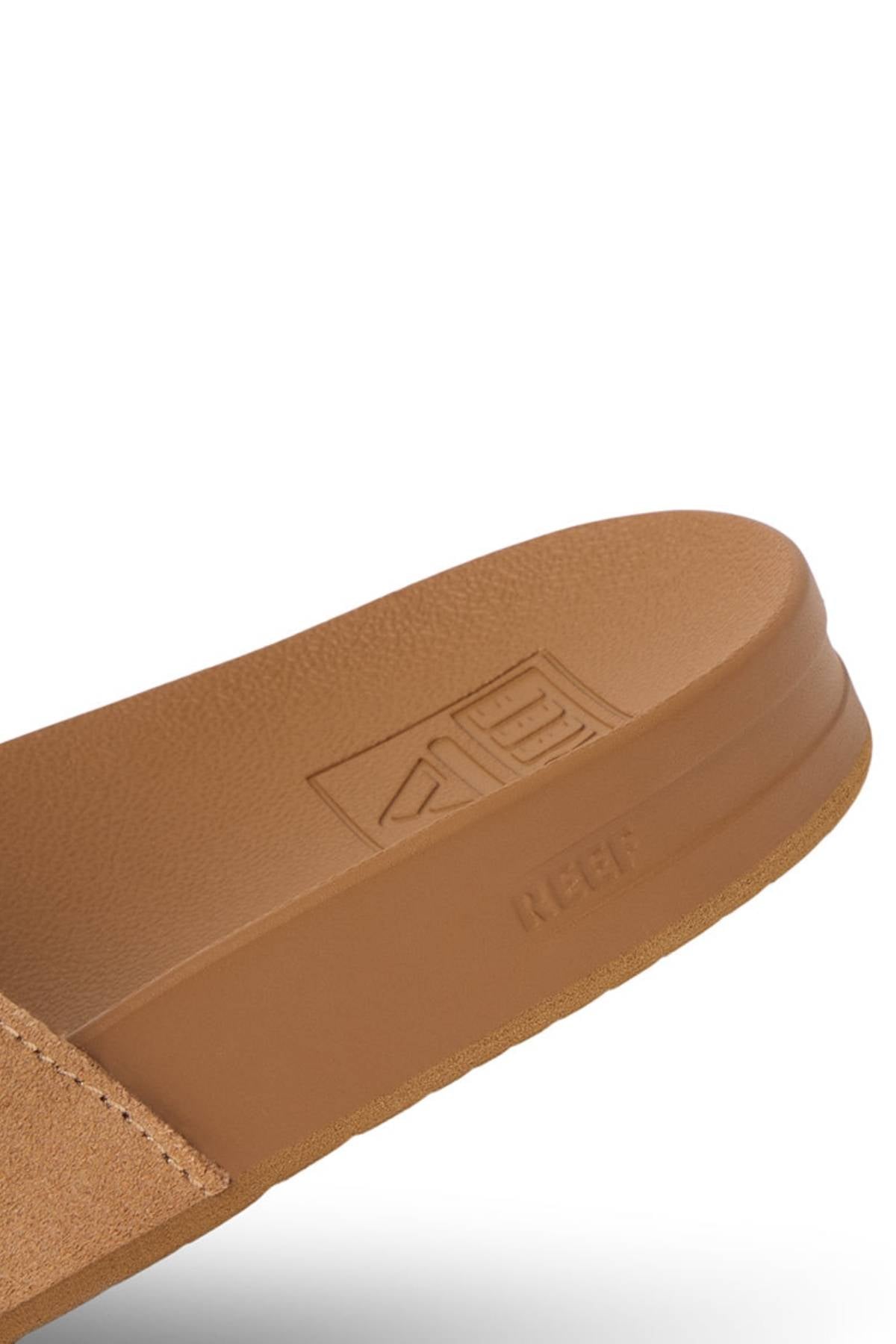 Close-up of the REEF Cushion Vista Stevie sandal in tan with suede straps, textured footbed, visible stitching, and "REEF" branding embossed on the strap and footbed. Features enhanced arch support for all-day comfort.