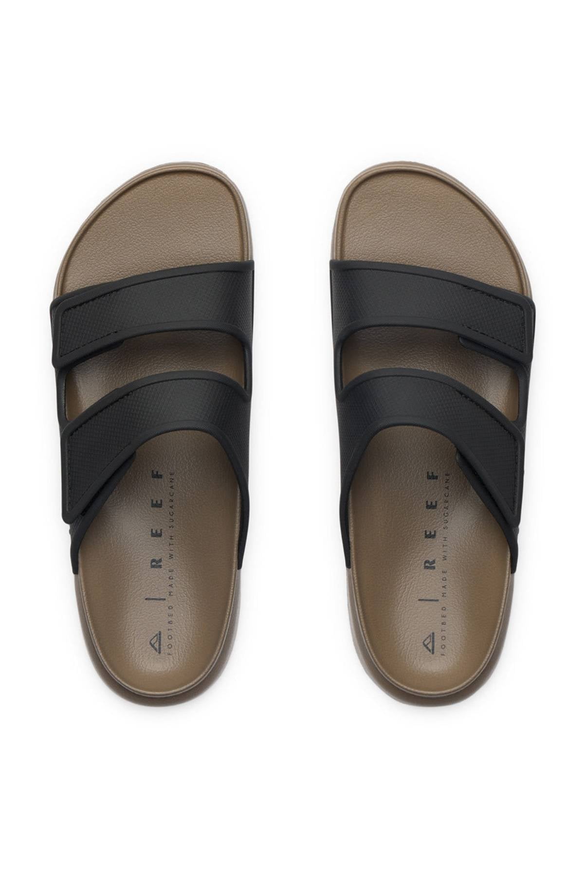 The REEF Oasis Adapt sandals feature two wide black adjustable straps on a brown base, "REEF" branding on the insole, and a cushioned EVA footbed for all-day comfort, displayed from above on a white background.
