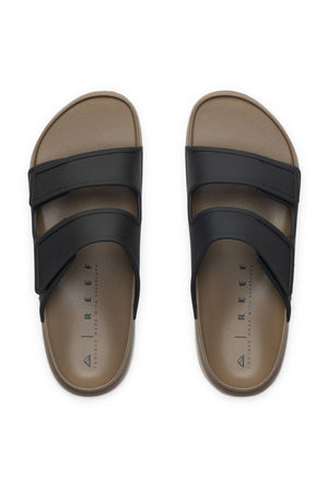 The REEF Oasis Adapt sandals feature two wide black adjustable straps on a brown base, "REEF" branding on the insole, and a cushioned EVA footbed for all-day comfort, displayed from above on a white background.