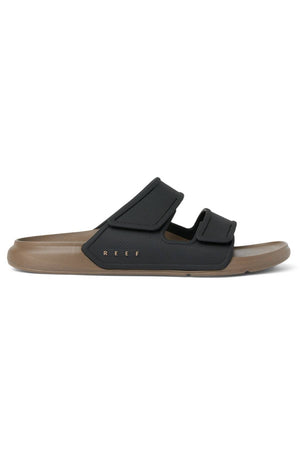 The REEF Oasis Adapt is a brown and black water-friendly slide sandal with two adjustable straps, "REEF" on the sole, an EVA footbed, open toe, and a casual design.