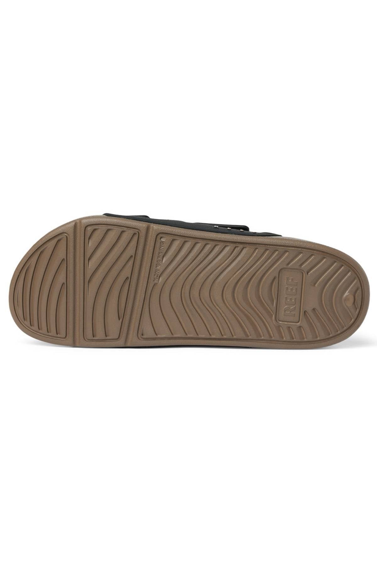 The image displays the sole of the REEF Oasis Adapt water-friendly slide sandal, featuring a tan rubber bottom with wavy tread patterns and "REEF" embossed near the heel, shown with the sole facing up.