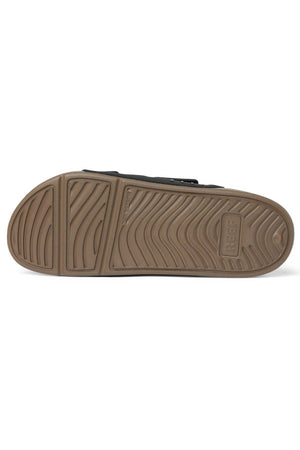 The image displays the sole of the REEF Oasis Adapt water-friendly slide sandal, featuring a tan rubber bottom with wavy tread patterns and "REEF" embossed near the heel, shown with the sole facing up.