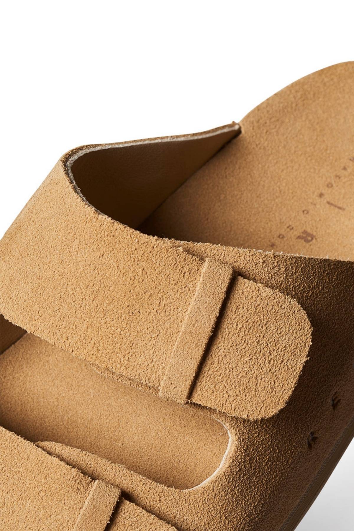 Close-up of the REEF Ojai Two Bar sandal in tan suede, featuring two wide straps with visible stitching and a soft, textured finish. Set against a white background, the image highlights the sandal’s supportive comfort and refined details.