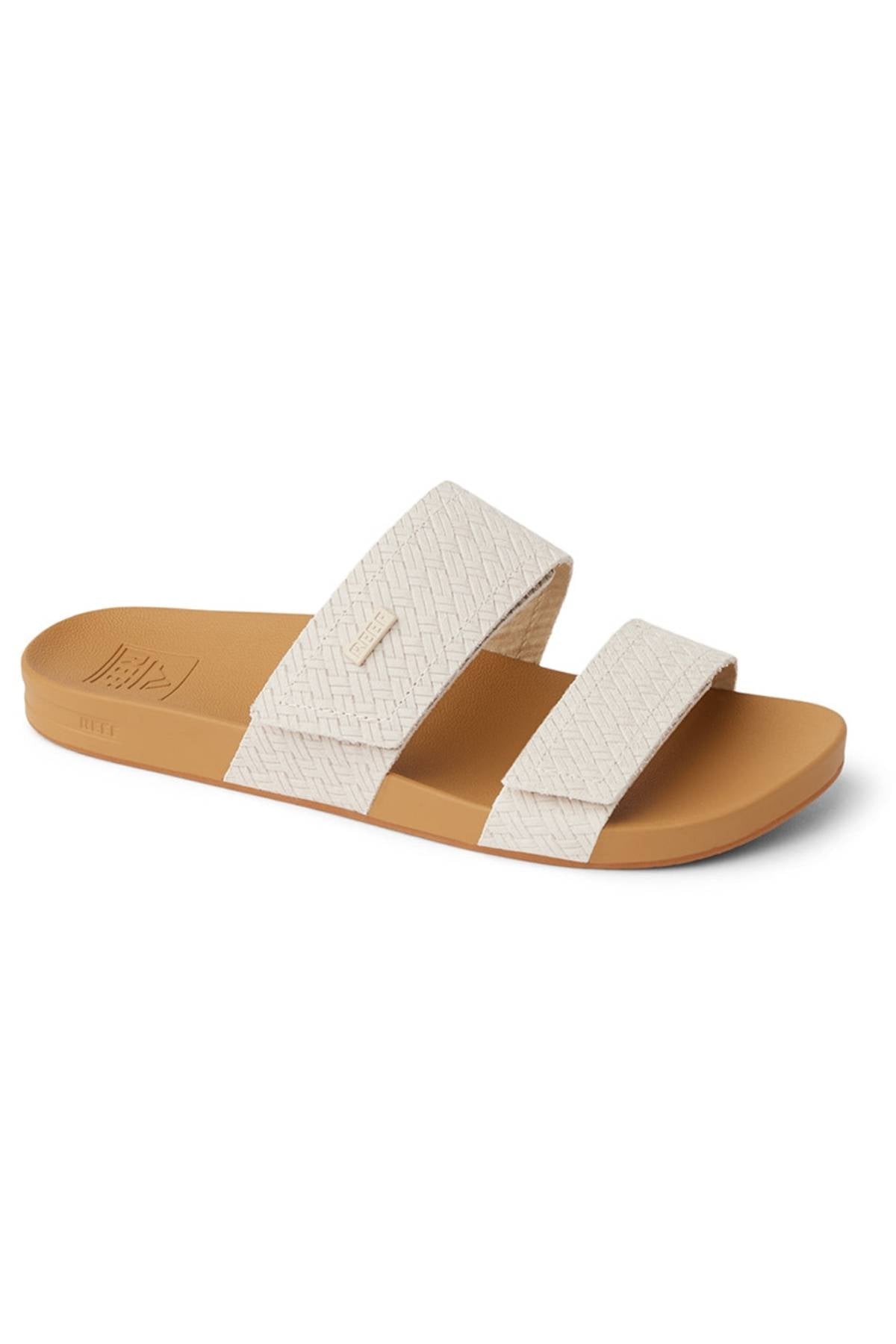 The REEF Velcro Vista Se is a tan slide sandal featuring two off-white textured straps, a flat sole, and a soft cushion midsole for all-day comfort. Enjoy its eco-friendly design, all showcased against a white background.
