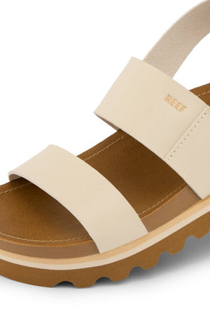 Close-up of the REEF Vista Hi Buckle sandal in beige vegan leather, featuring two wide straps, an ankle strap, a brown textured sole with "REEF" on the side strap—stylish platform sandals with added arch support.