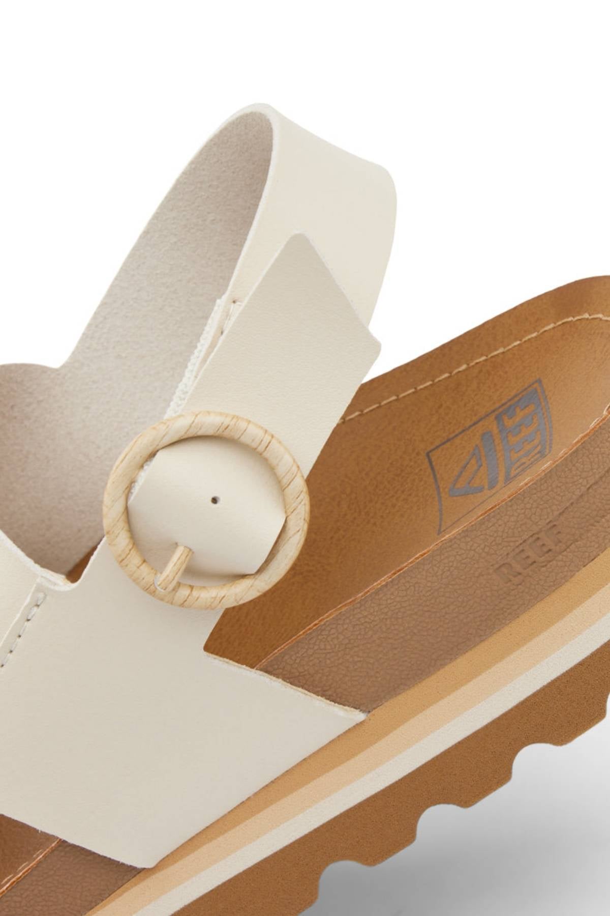 Close-up of the REEF Vista Hi Buckle sandal in beige vegan leather, with a thick platform sole, supportive tan footbed, wide strap, round textured buckle, and visible REEF logo on the inner footbed.