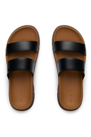 The REEF Vista Luxe Thea sandals shown side by side feature two wide black vegan leather straps and a comfortable footbed on a brown slide, displayed against a white background.