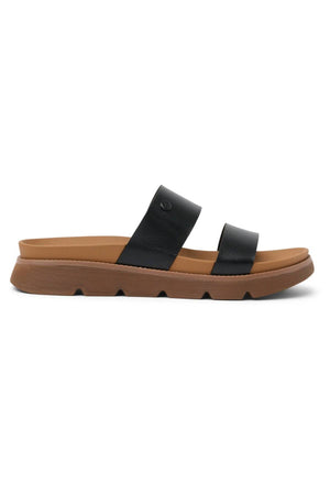 The REEF Vista Luxe Thea sandal features a light brown sole and two wide black vegan leather straps, combining durability and style. Shown in a side profile against a white background.