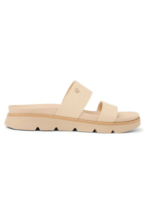 The REEF Vista Luxe Thea is a beige slip-on sandal with two wide straps, a thick ridged sole, a cushioned footbed, and vegan leather construction, shown in side profile against a white background.