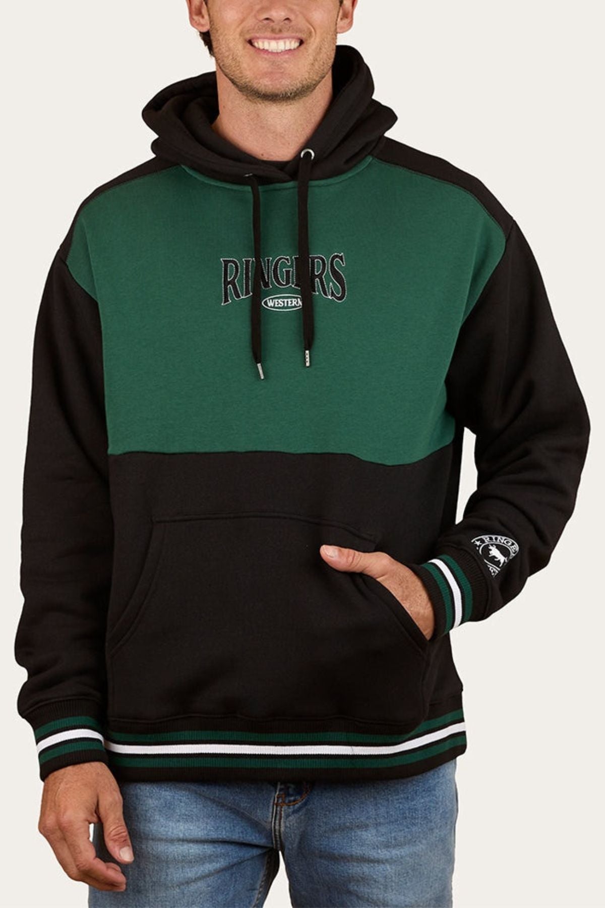 Someone wearing a green and black Ringers Western Barrow Creek Pullover Hoodie with "RINGERS WESTERN" on the chest, an embroidered sleeve patch, front pocket, drawstrings, and paired with blue jeans.