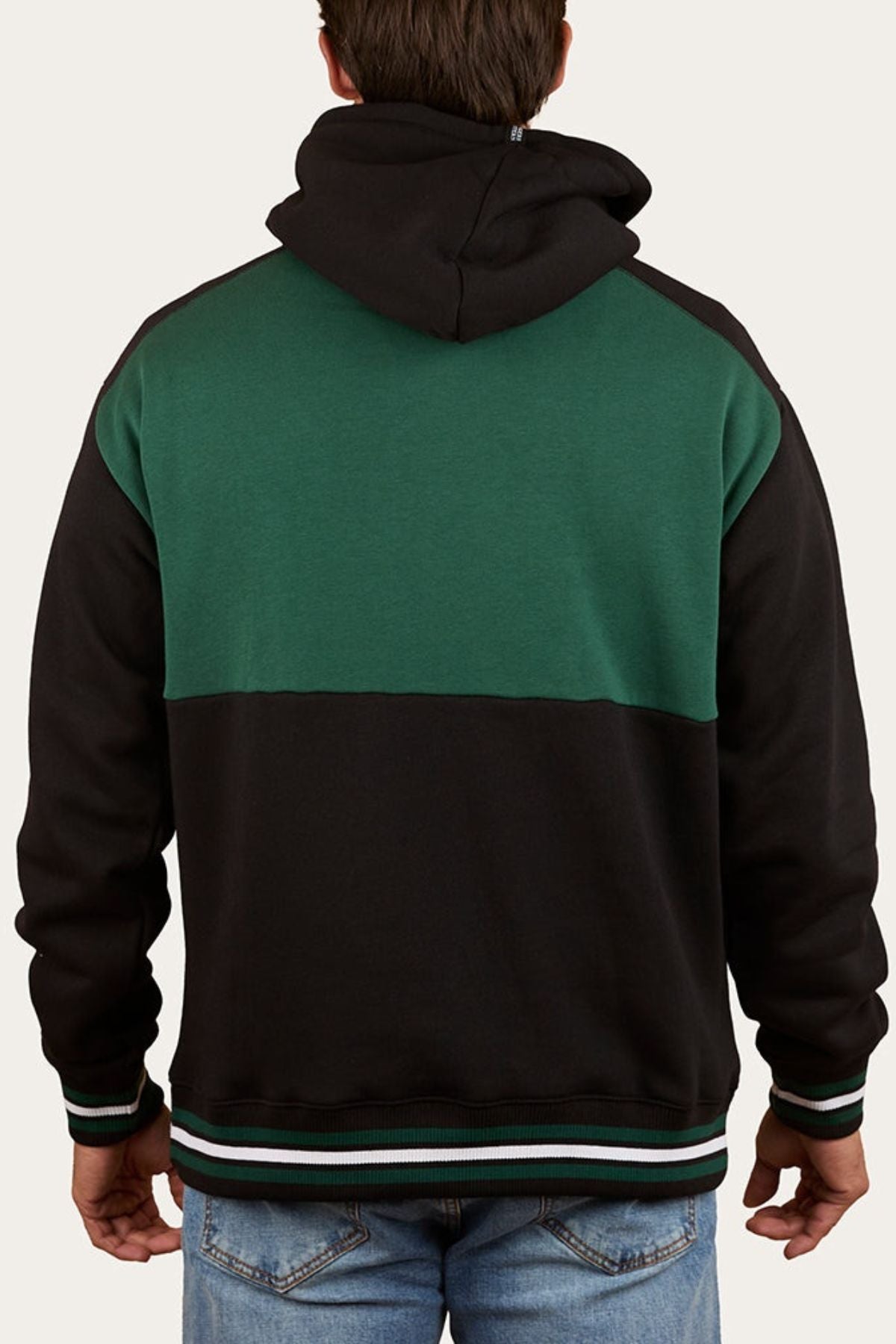 A person is seen from the back wearing the Ringers Western Barrow Creek Pullover Hoodie, black and green with striped cuffs and waistband, hood down on their shoulders, paired with blue jeans.