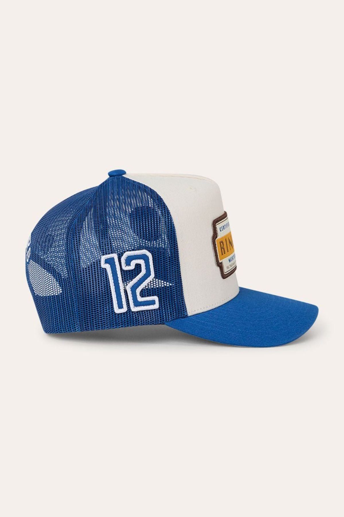 The Ringers Western Drive By Deep Fit Trucker Cap is a blue and white trucker hat with a mesh back, offering sun protection, the number 12 on the side, a deep fit design, and a rectangular embroidered patch on the front.