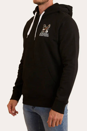 A man wears the Ringers Western Eyrie Pullover Hoodie—black brushed fleece with white drawstrings, front pocket, and a small "Ringers Western" eagle graphic on the left chest—paired with relaxed fit blue jeans.