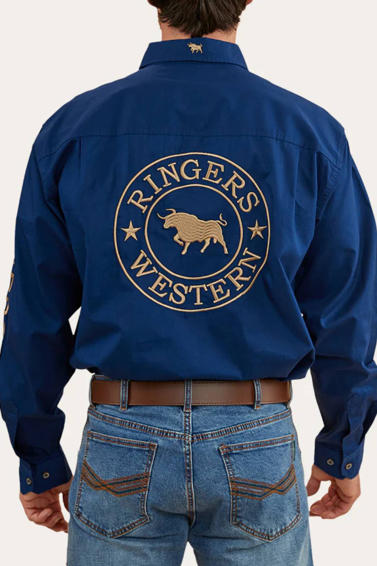 A person is shown from behind wearing a blue Ringers Western Hawkeye Embroidered Shirt with UPF50+ protection and a gold bull on the back, paired with blue jeans and a brown belt.