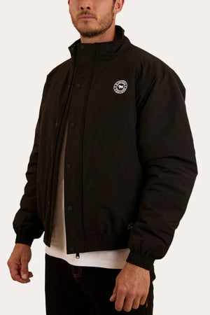 A man wears the black Ringers Western Kidman Jacket, featuring a small circular logo on the left chest, elastic cuffs, and DWR coating over a white shirt, styled simply against a plain background.