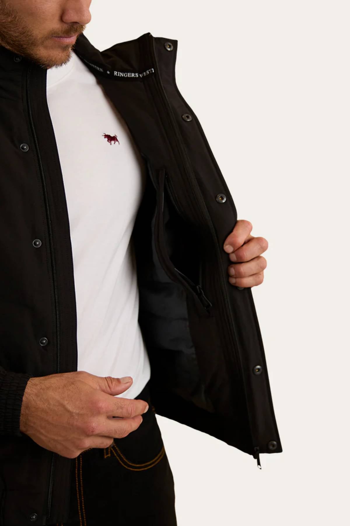 A man wearing a white t-shirt and the Ringers Western Kidman Jacket opens it to reveal its quilted lining and inner zip pocket. Only his torso and part of his face are visible.