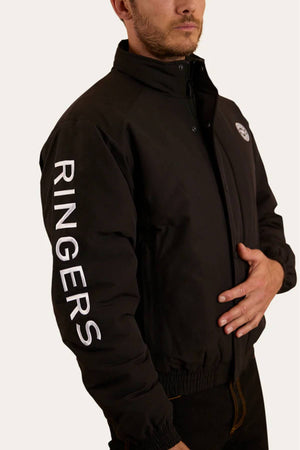 A man wears the Ringers Western Kidman Jacket, a black high-collared piece with "RINGERS" in bold white letters down the sleeve and a quilted lining. He has one hand in his pocket and faces slightly away from the camera.