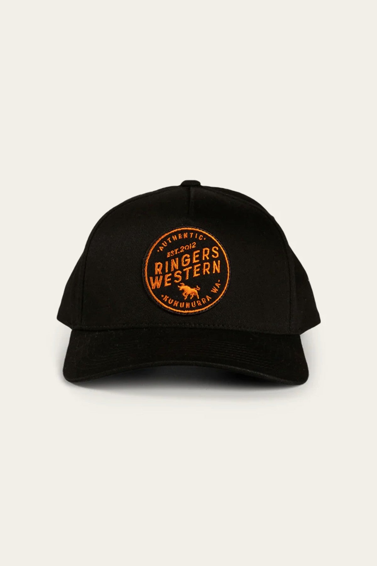 Introducing the Ringers Western Rye Baseball Cap: A black cotton twill baseball cap adorned with an orange circle patch on the front. The patch features the text "Authentic Ringers Western" along with a small emblem of a bull against a plain, off-white background.
