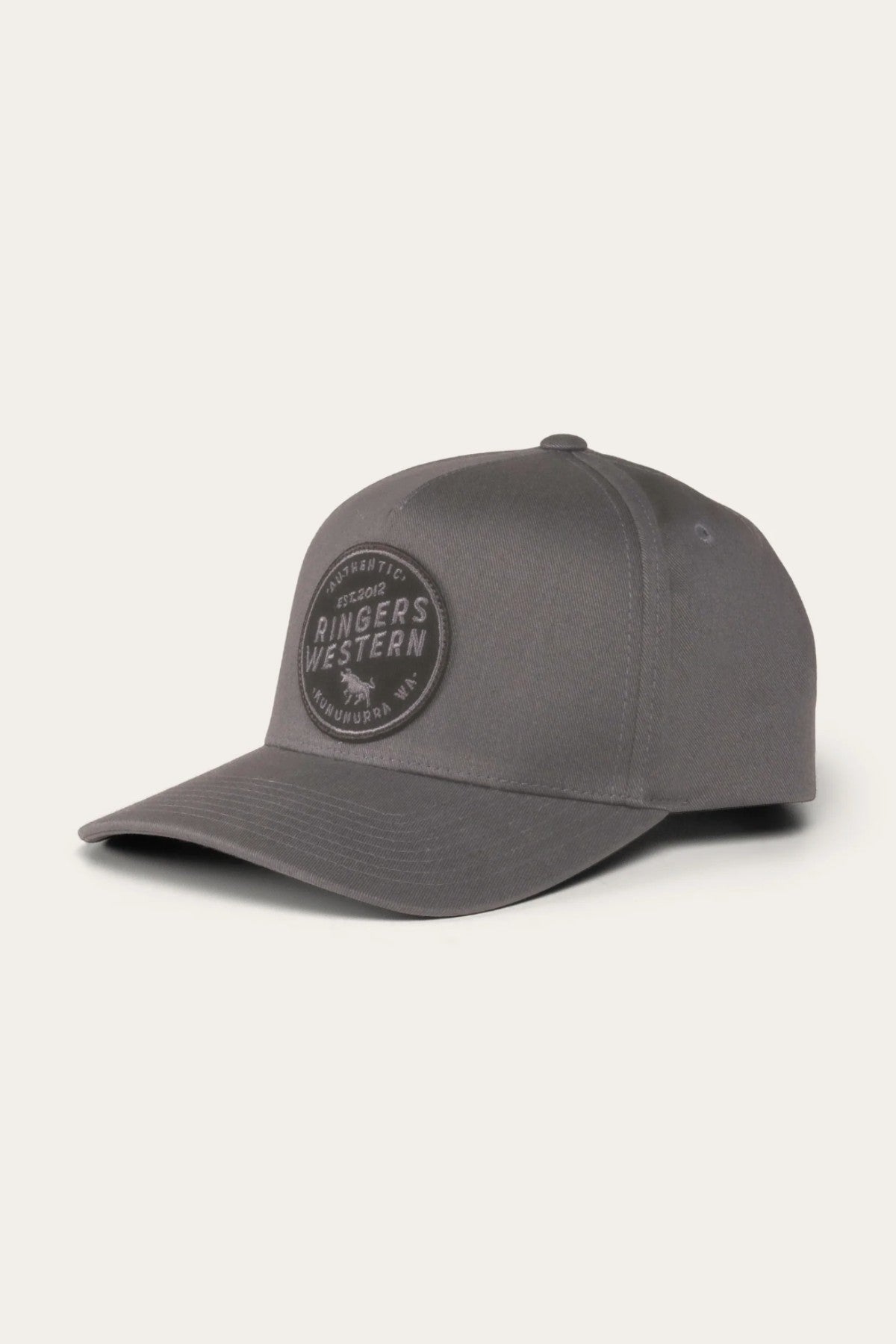 The Ringers Western Rye Baseball Cap is a gray cap crafted from cotton twill. It features a curved brim, eyelets for ventilation, and a black circular patch on the front displaying the words "Ringers Western.