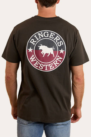 A man stands with his back to the camera, wearing a black Ringers Western Signature Bull Loose Fit T-Shirt featuring a large circular bull and stars logo on the back. Made from 100% Cotton Jersey, it pairs perfectly with blue jeans.