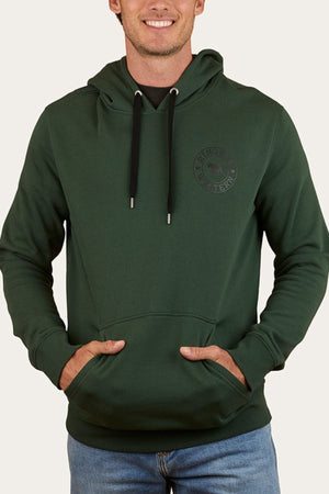 A man wears the Ringers Western Signature Bull Pullover Hoodie in dark green with black drawstrings and a small logo on the left chest, hands in front pocket, styled with blue jeans for a relaxed look.