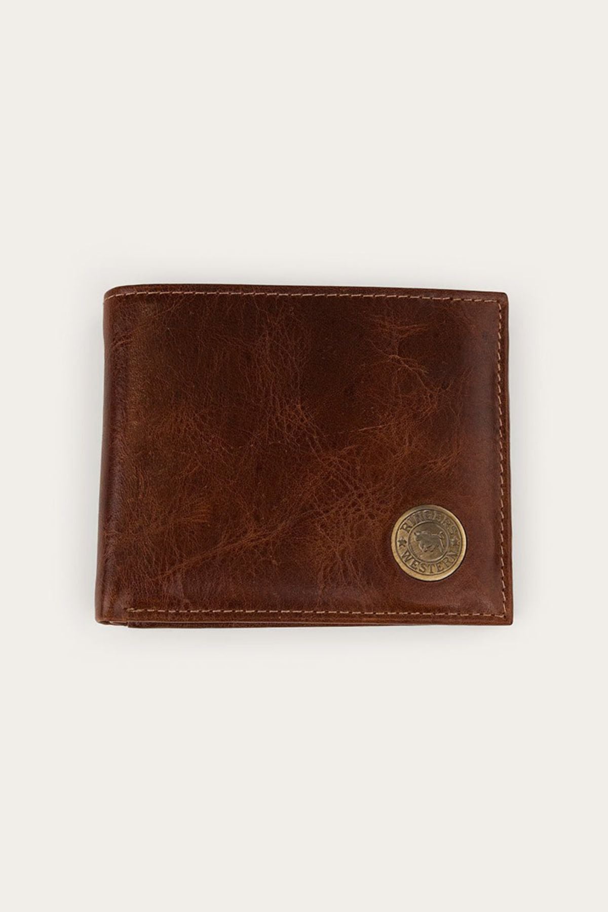 The Ringers Western Toro Biggo Wallet, crafted from brown pull-up leather with visible stitching and finished with a round brass emblem in the lower right corner, is displayed against a plain light background. This wallet combines classic style with enhanced durability for everyday use.