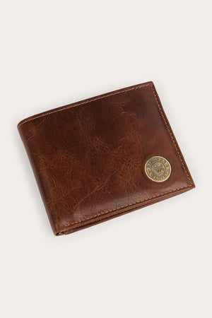 The Ringers Western Toro Biggo Wallet, crafted from brown pull-up leather with visible stitching and featuring a round gold emblem in the lower right corner, is displayed against a light beige background.