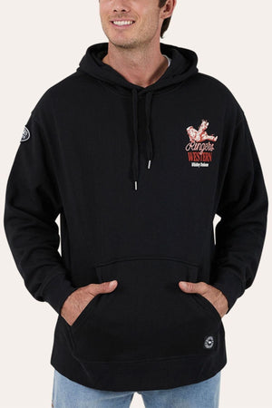 A man smiles with his hands in the pocket of a black Ringers Western Whiskey Business Pullover Hoodie, which has brushed fleece, a front pocket, and a small red and white embroidered chest logo.