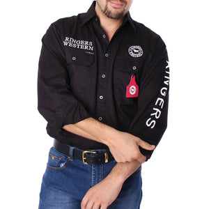 The man confidently wears a Ringers Western Hawkeye Embroidered Shirt, black and button-up with UPF50+, featuring the brand's logo on the chest and sleeve. Paired stylishly with blue jeans and a black belt, his arms are crossed in front, completing the rugged ensemble.