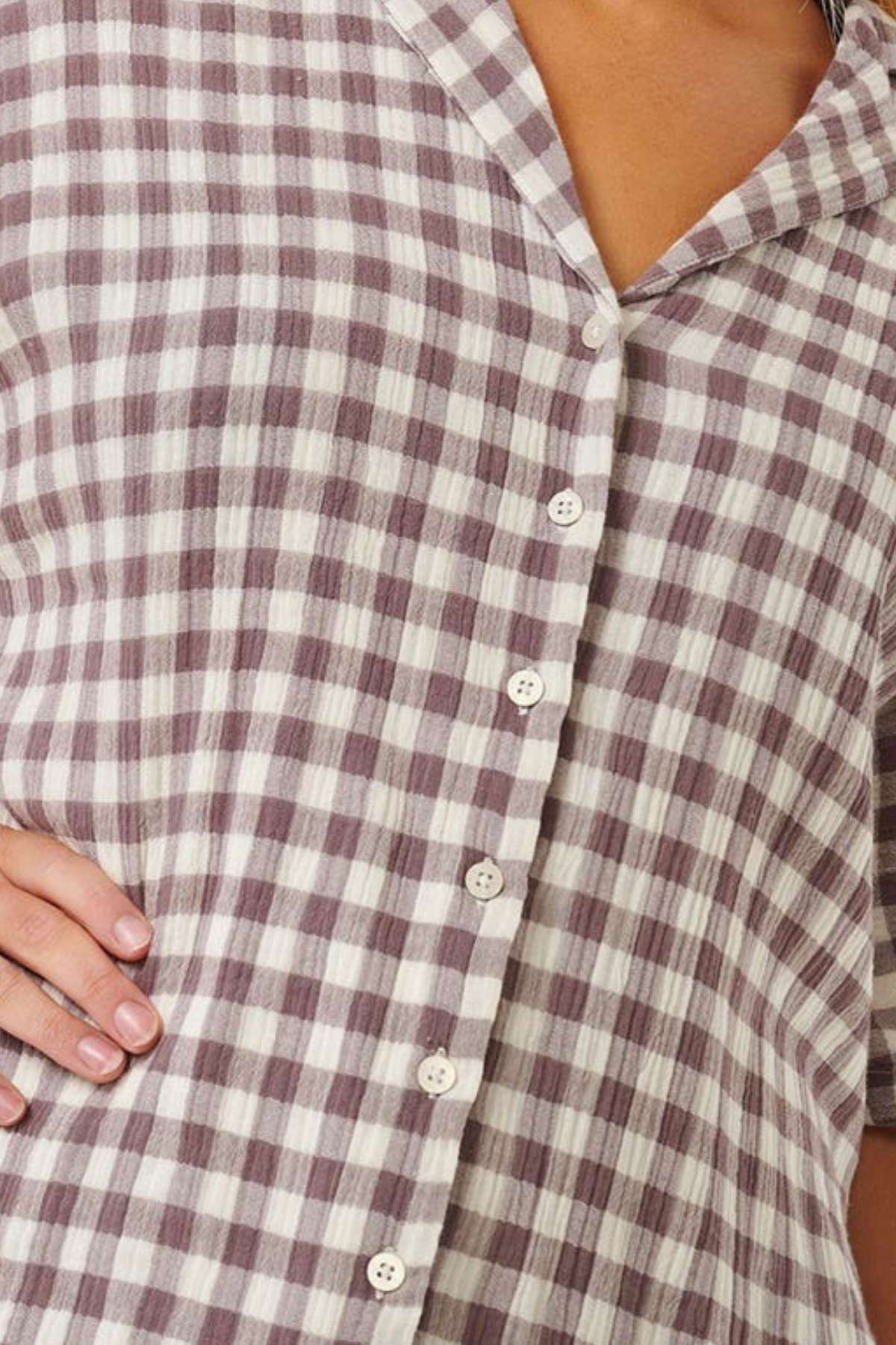 Close-up of an ocean enthusiast wearing a button-up Rip Curl Premium Surf Check Shirt featuring a checkered pattern in brown and white. One hand is placed on their hip, highlighting the collar and buttons along the front. The textured fabric is made from 100% cotton.