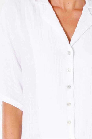 Close-up of a person wearing a white Rip Curl Premium Surf Shirt with a relaxed fit. The short-sleeve shirt, made from cotton double weave gauze fabric, features a soft collar and appears lightweight. Only the upper torso is visible, without any background details.