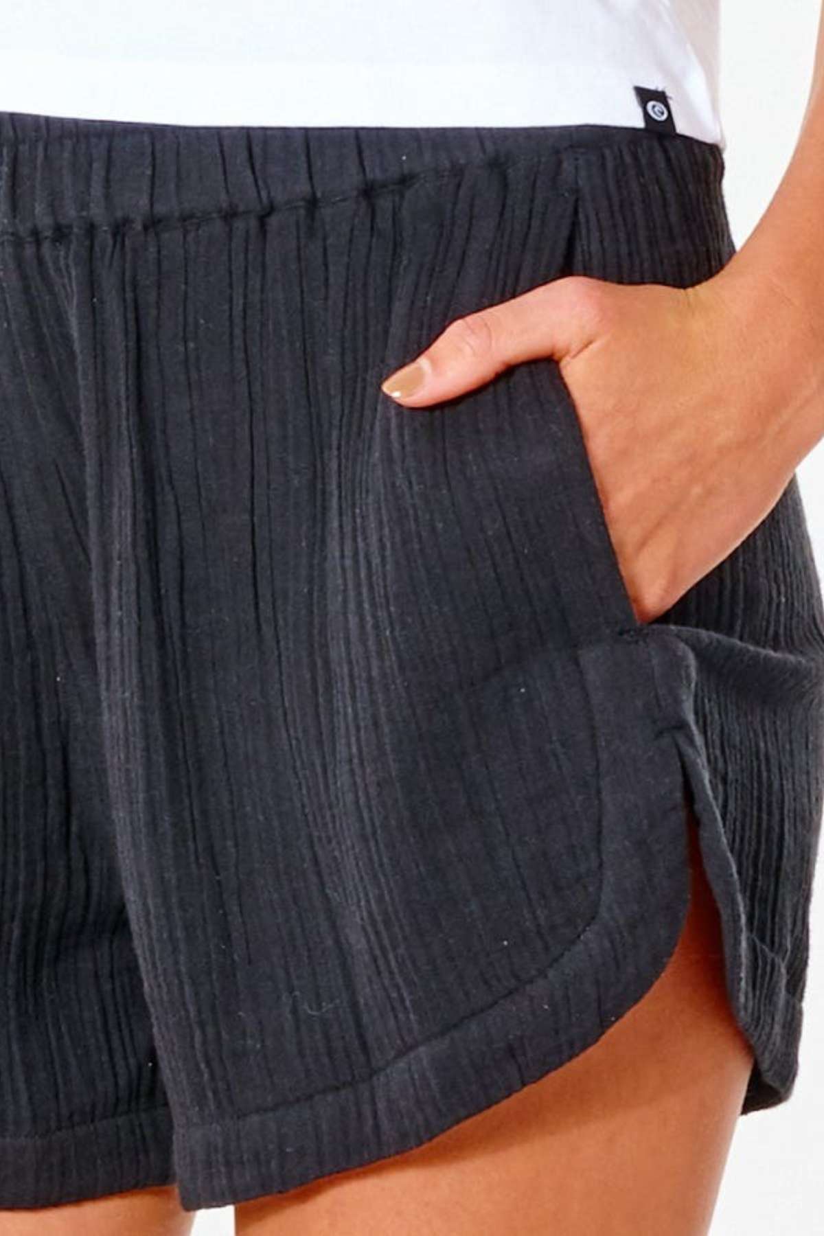Close-up of a surf enthusiast sporting the Rip Curl Premium Surf Short in textured black, featuring a hand in the pocket. The shorts display a subtle stripe pattern and a small side slit, complementing the white top flawlessly.