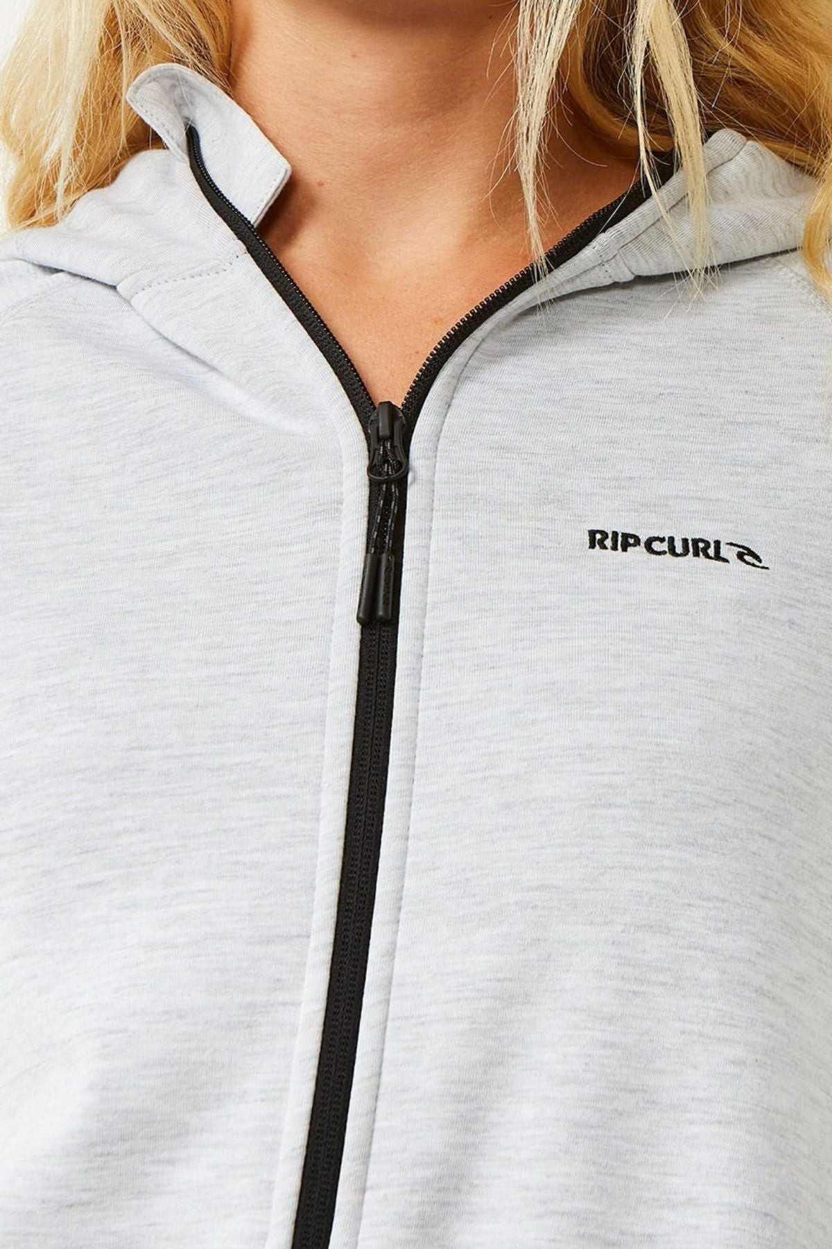 Close-up of a person wearing the Rip Curl Anti Series Flux III Jacket in light gray, featuring a black zipper and "RIP CURL" logo on the left chest; this lightweight, shower-resistant jacket ensures style and comfort.